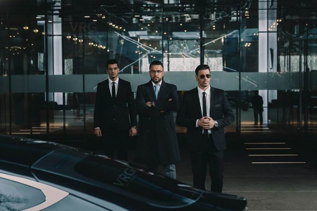 Siyah takım elbiseli, profesyonel VRG yakın koruma ekibi, lüks transfer aracı önünde duruyor. Yüksek seviye özel güvenlik hizmetleri.